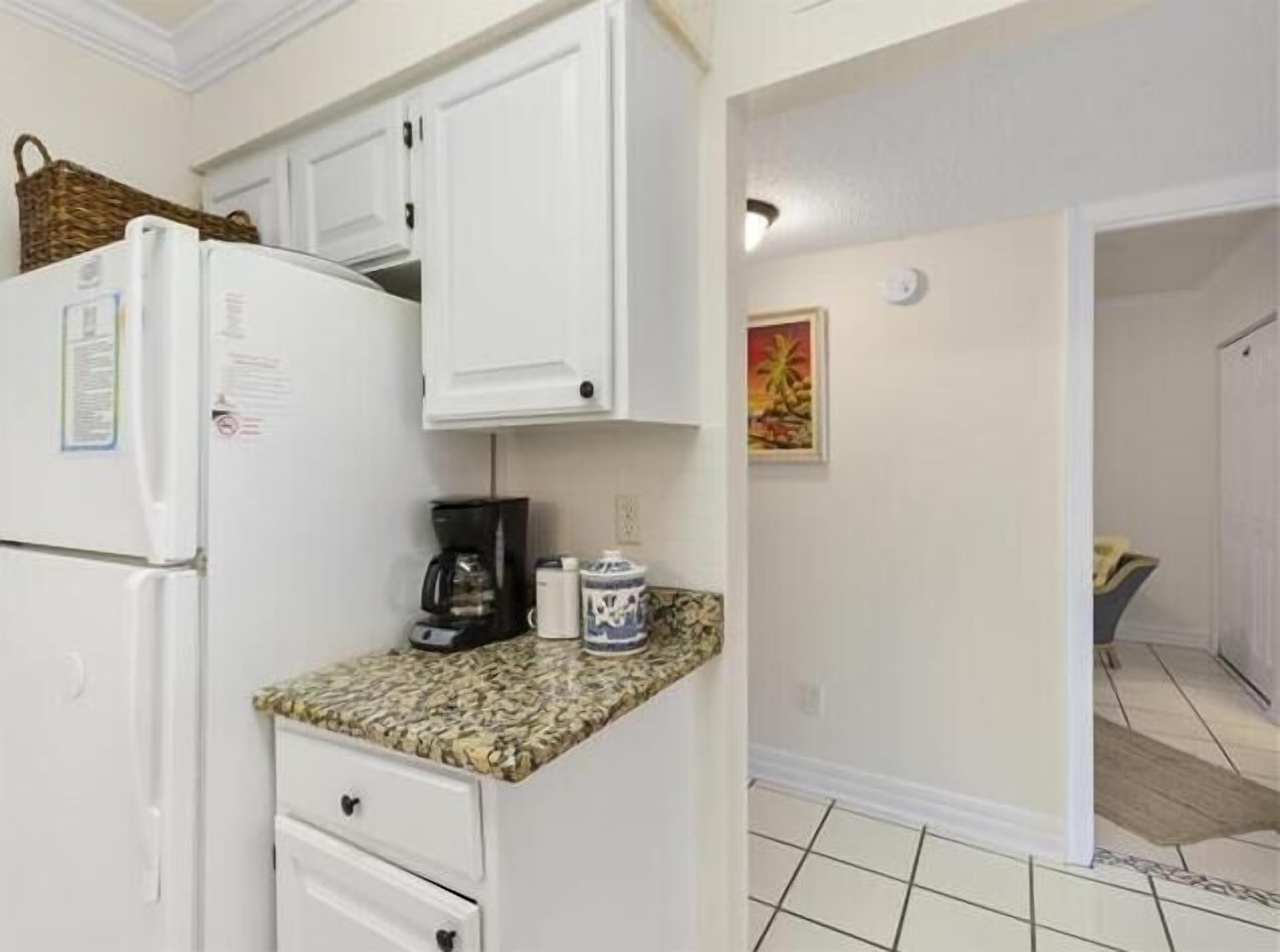 A compact kitchen with white cabinets, a refrigerator, a coffee maker, and a microwave.