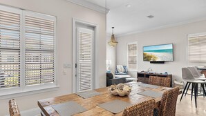 A dining area with a wooden table, woven chairs, and a television displaying a beach scene. - Sugar Sands (Miramar Beach)
