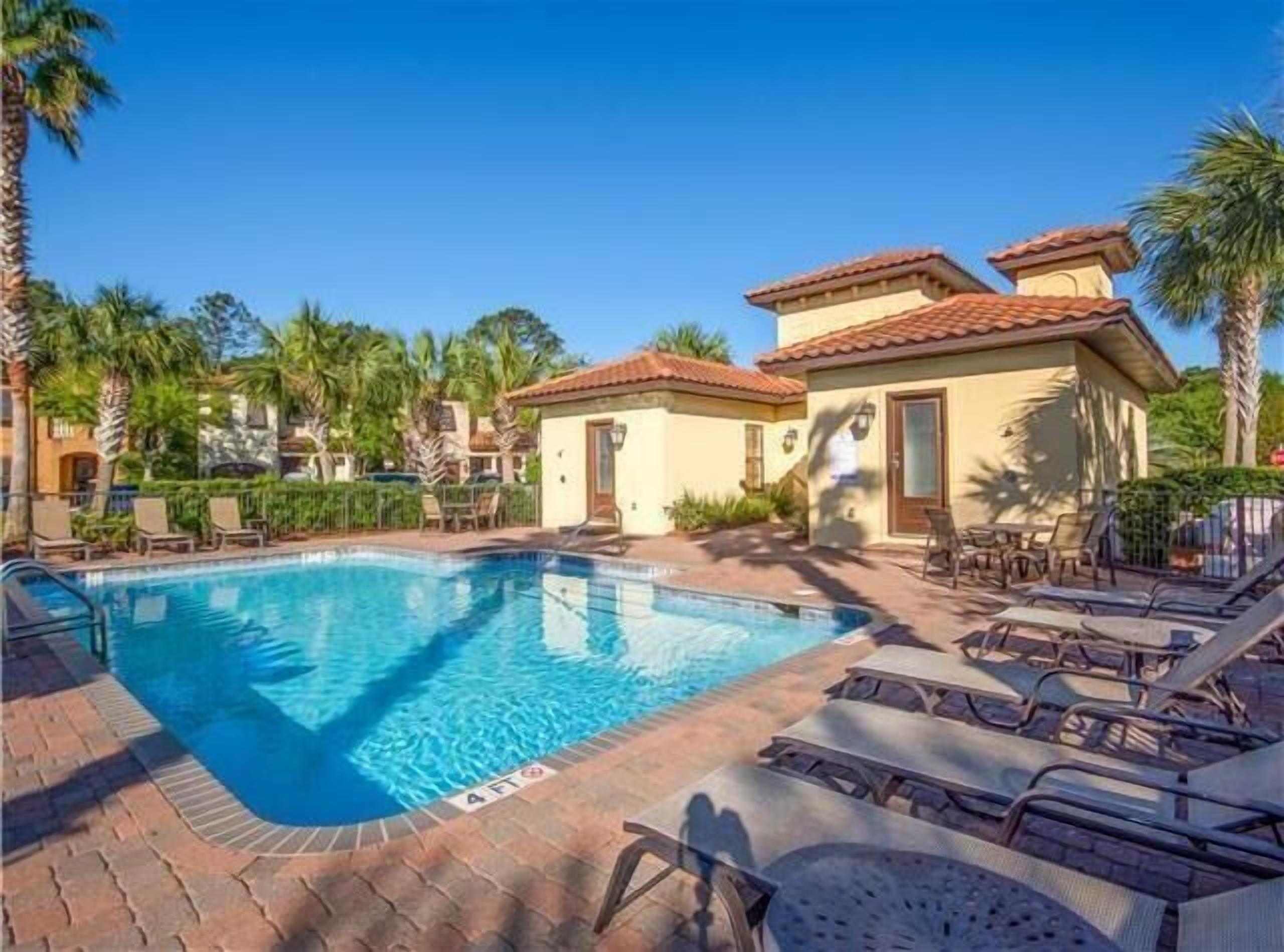 A swimming pool with lounge chairs, a building with a tiled roof, and palm trees.