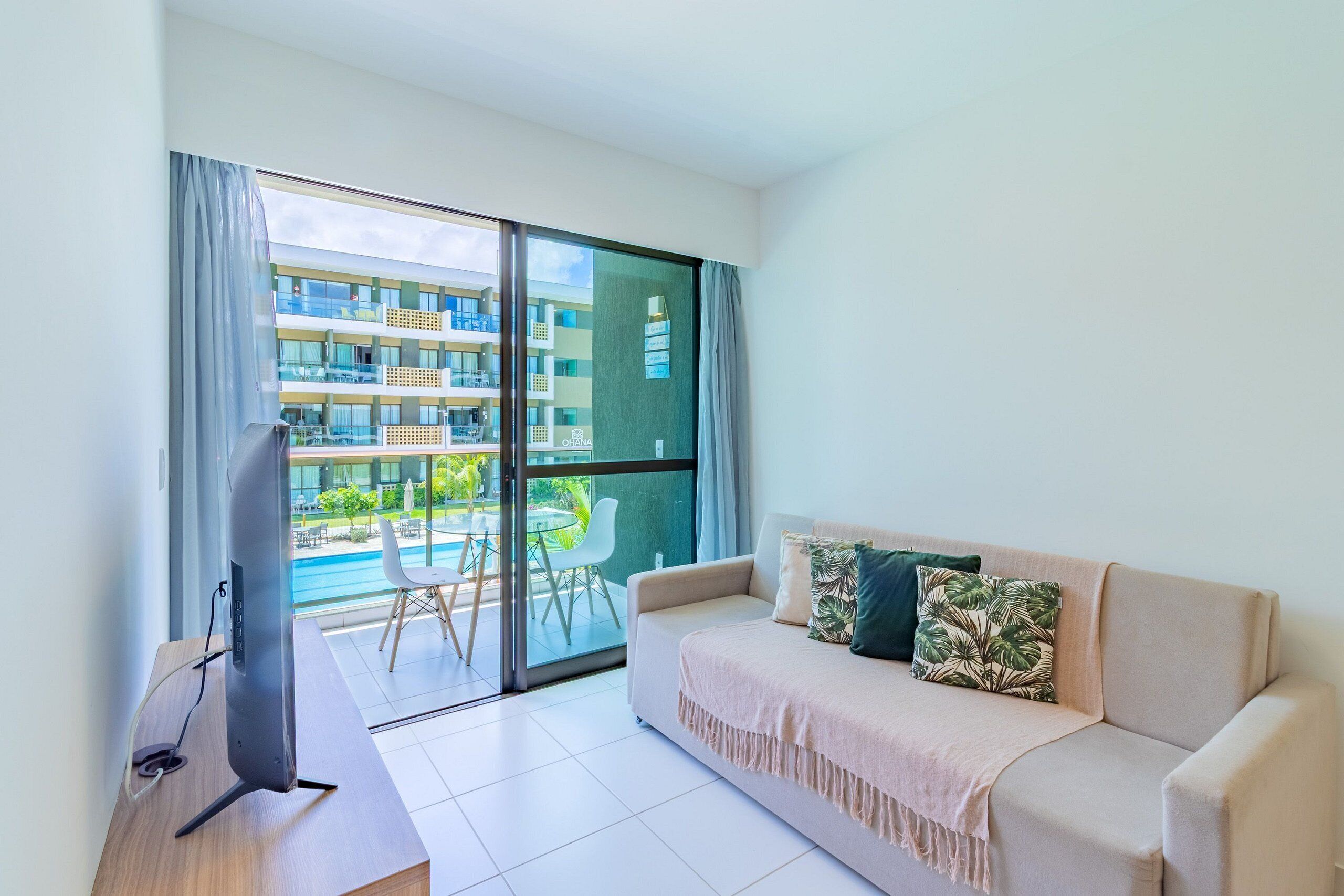 Sala de estar moderna com sofá, TV de tela plana e varanda com vista para a piscina.