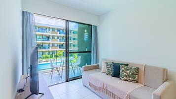 Sala de estar moderna com sofá, TV de tela plana e varanda com vista para a piscina.