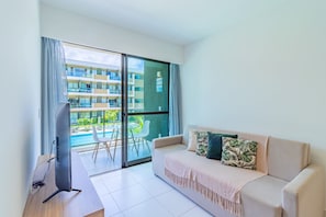 Ein modernes Wohnzimmer mit einer Couch, einem Flachbildfernseher und einem Balkon mit Blick auf einen Pool.