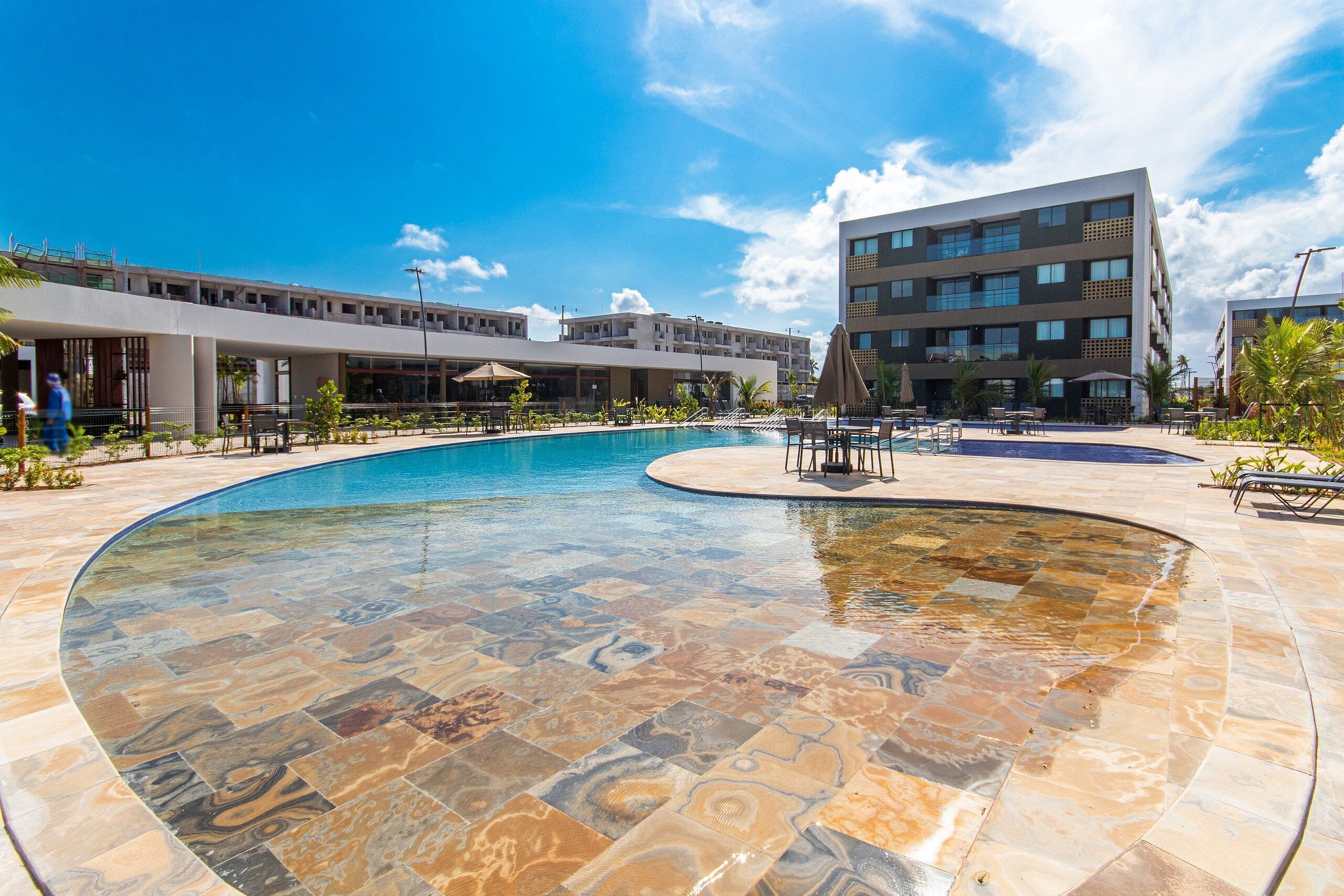 Piscina com um design de azulejos único, rodeada por um edifício moderno com vários andares e varandas.