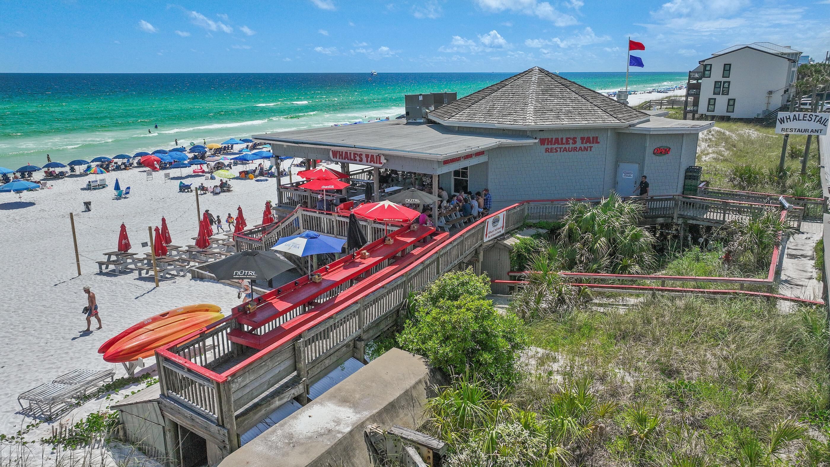 A beachside restaurant with a view of the ocean, outdoor seating, and a lifeguard stand.