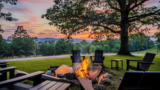 Ein Lagerfeuer mit Sitzgelegenheiten, umgeben von Bäumen und Blick auf den Sonnenuntergang.