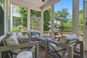 A covered porch with outdoor furniture, large windows, and a view of greenery and buildings. - East Royal | Including Golf Cart & Water Color Beach Club (Santa Rosa Beach)