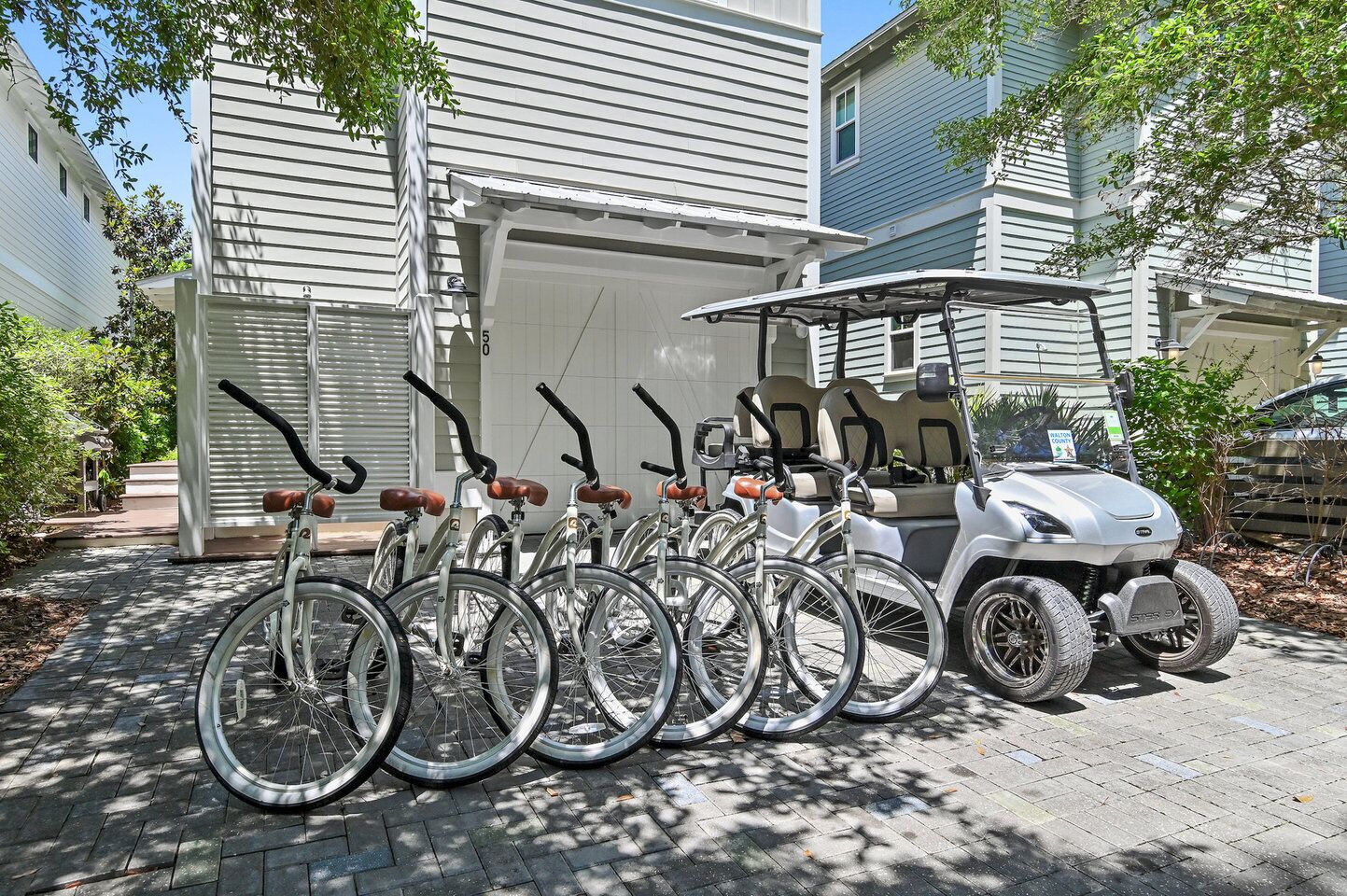 Een rij fietsen geparkeerd voor een gebouw met een garage, een golfkar en een pad van stenen.