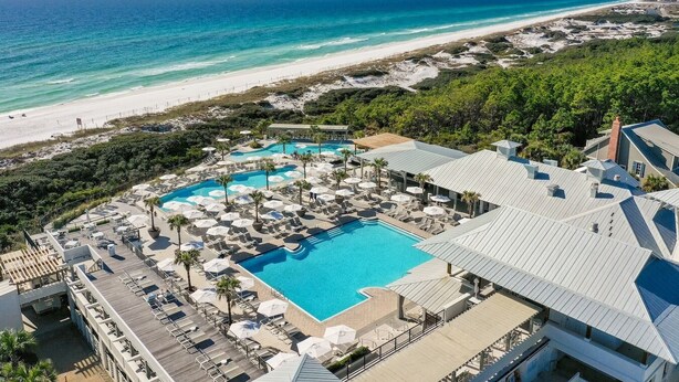 Un resort con una piscina grande, sillas de descanso y vista al mar.
