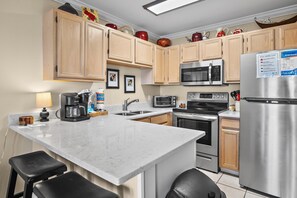 A kitchen with wooden cabinets, a stainless steel refrigerator, a microwave, and a coffee maker. - Summerspell 305 (Miramar Beach)