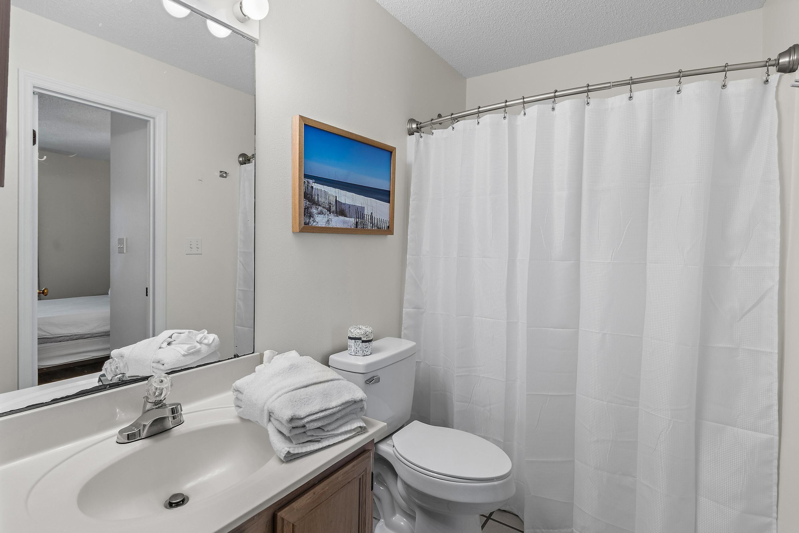 A bathroom with a sink, mirror, toilet, and shower curtain.