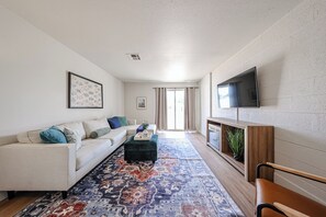 Ein Wohnzimmer mit einer Couch, Hocker, Fernseher und einem gemusterten Teppich.