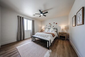 Ein Schlafzimmer mit einem Bett, Nachttischen, einer Bank, einem Deckenventilator und einem Fenster mit Vorhängen.