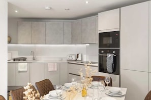 Cocina moderna con armarios grises, horno empotrado y un comedor con mesa dispuesta para dos.