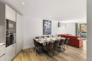 Una cocina moderna con muebles blancos, una mesa de comedor para seis personas y un sofá rojo en la sala de estar.