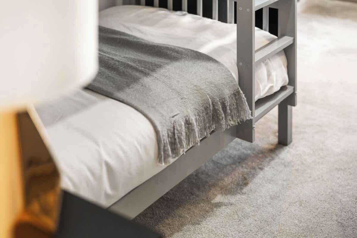 Uma cama de beliche com colchão e cobertor cinzas.
