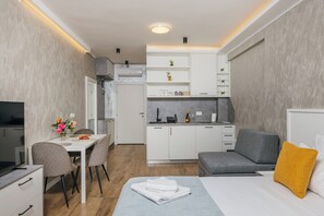 Una habitación de hotel compacta con cama, escritorio, kitchenette y zona de estar.