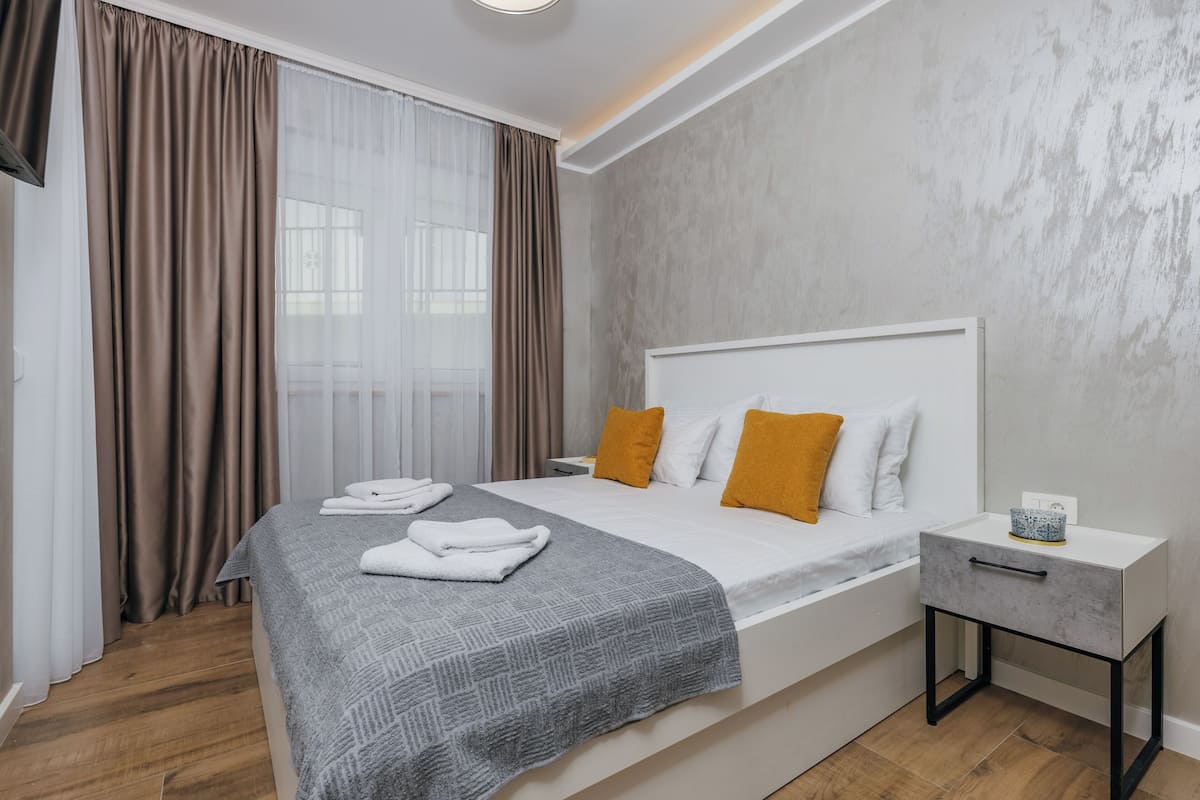 A modern hotel room with a large bed, a bedside table, and a view through sheer curtains.