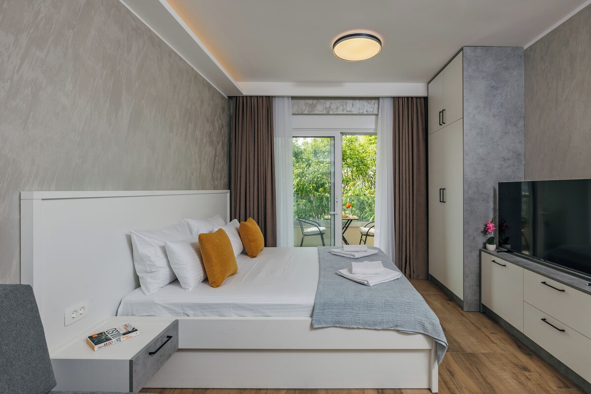 A modern hotel room with a bed, a TV, a desk, and a balcony with a view.