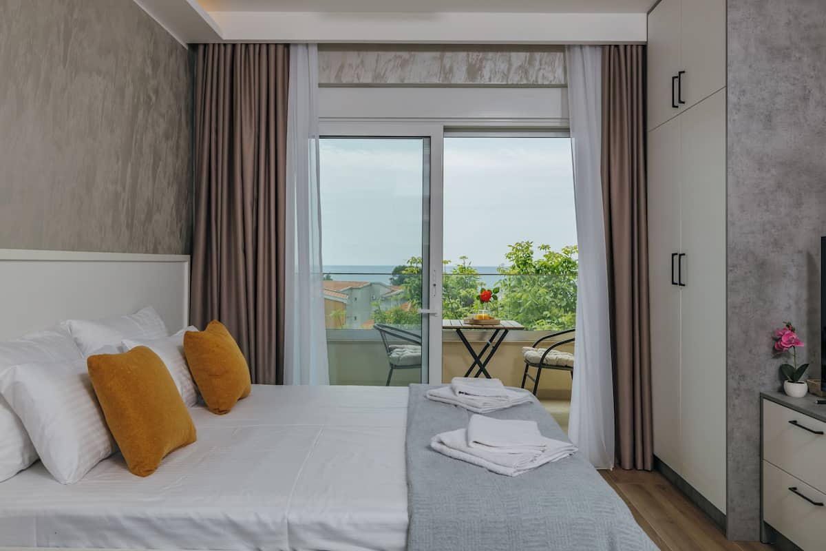 A hotel room with a bed, a balcony with a table and chairs, and a view of the sea.