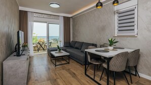 Una sala de estar moderna con sofá, mesa de comedor y sillas, televisión y un balcón con vistas.