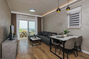 Una sala de estar moderna con sofá, mesa de comedor y sillas, televisión y un balcón con vistas.