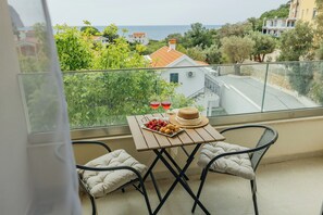A balcony with a table, two chairs, a hat, and a tray of food and drinks. - Apartments Via Mare (Petrovac)