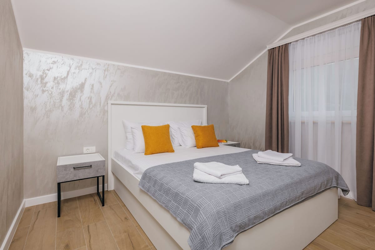 A modern hotel room with a large bed, a bedside table, and a window with curtains.