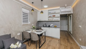 Una cocina compacta con armarios blancos, una mesa de comedor con sillas e iluminación colgante.