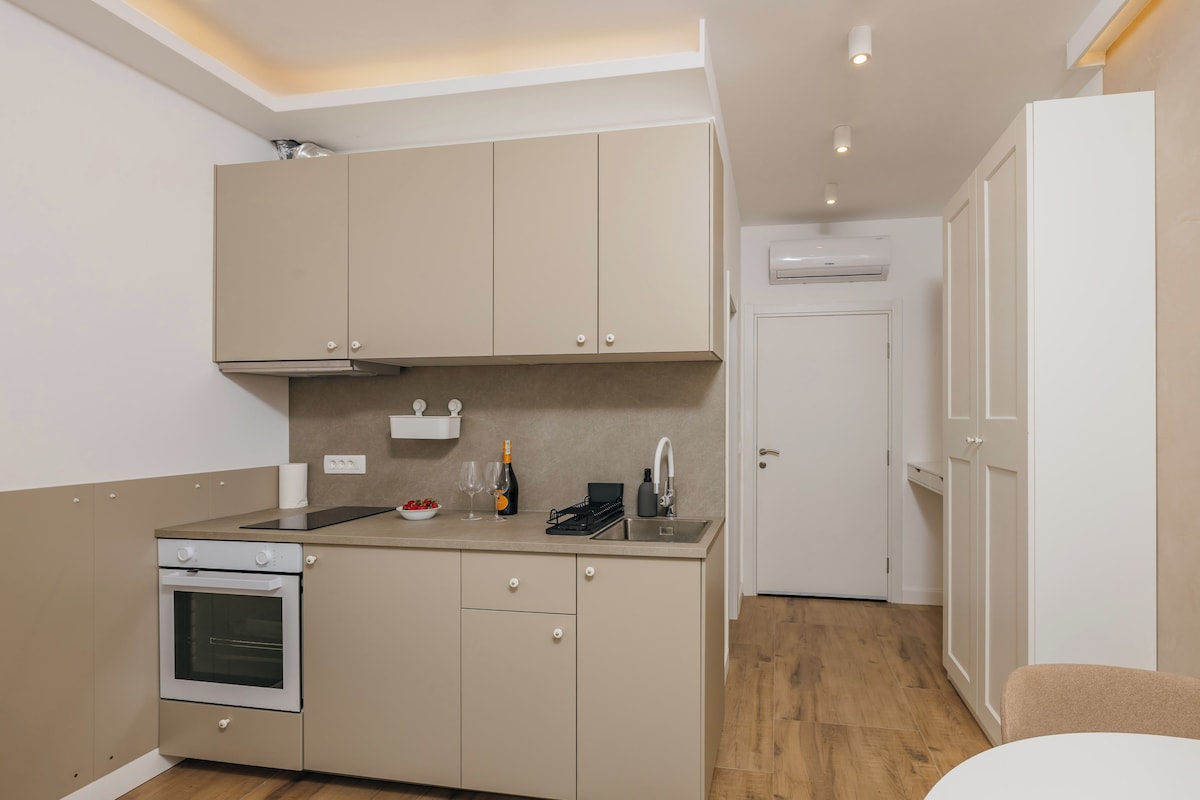 Una cocina compacta con horno integrado, un lavamanos y una encimera con una botella y vasos.