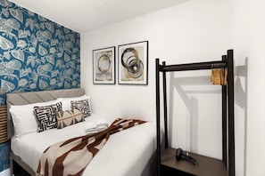 Ein Schlafzimmer mit einem Bett, Kissen, einer Decke, einer Holzbank und zwei gerahmten Kunstwerken an der Wand.