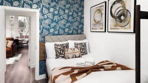 Une chambre à coucher avec un papier peint à motifs, un lit recouvert d’une couverture marron et blanche, et deux œuvres d’art encadrées accrochées au mur.