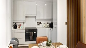 Une cuisine de taille réduite avec des meubles blancs, une table à manger avec des chaises et un panneau en bois sur le côté droit.