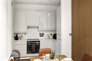 A compact kitchen with white cabinetry, a dining table with chairs, and a wooden panel on the right. - London home w/ dining & pet-friendly stay (Greater London)