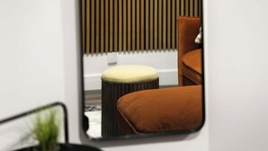 Une pièce dans laquelle un miroir reflète un fauteuil marron et un petit tabouret avec un coussin.