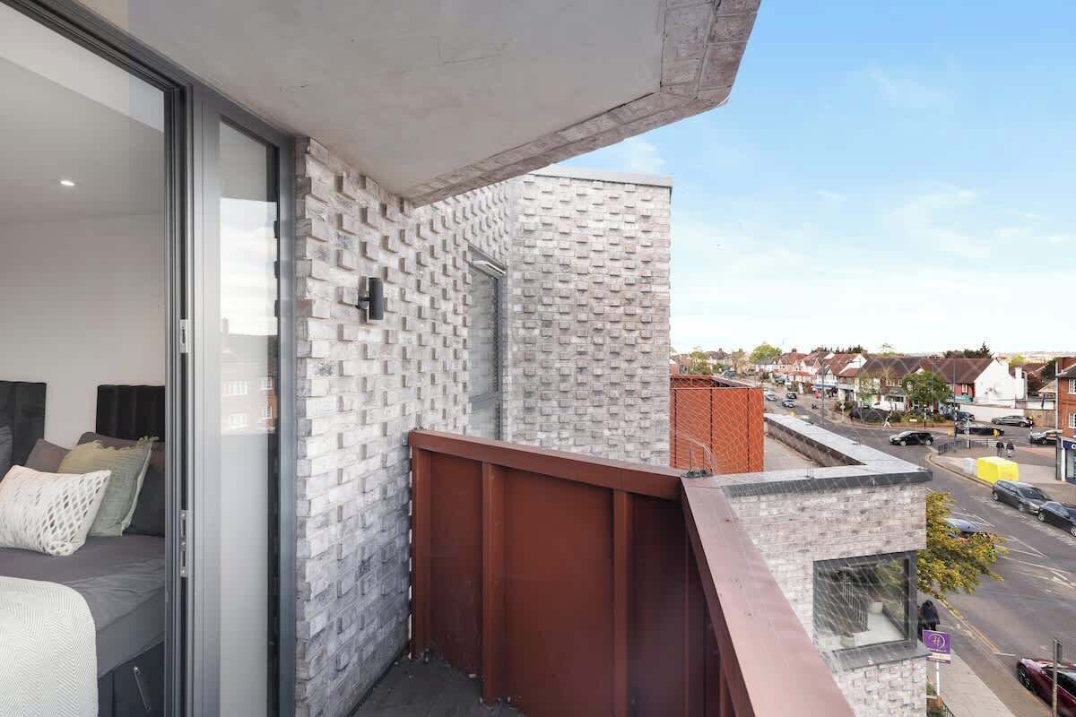 A balcony with a brick wall, a metal railing, and a view of the street.