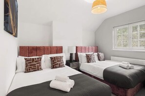 Hotellihuone, jossa on kaksi sänkyä, ikkuna, jossa on sälekaihtimet, lamppu ja taulu seinällä.