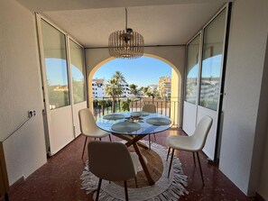 A balcony with a glass table and chairs, a woven rug, and a hanging light fixture.
