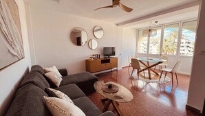 Una sala de estar con sofá, televisor, mesa de comedor, sillas y ventilador de techo.