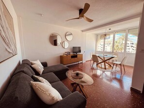 Un soggiorno con divano, televisore, tavolo da pranzo, sedie e ventilatore a soffitto.