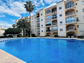 Un hotel de varios pisos con balcones, piscina y palmeras.