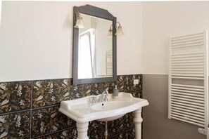 Un baño con un lavamanos blanco, un espejo con dos luces y un perchero para toallas.