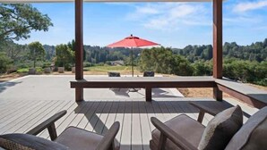 Eine überdachte Terrasse mit Holzmöbeln und einem roten Sonnenschirm, mit Blick auf eine bewaldete Landschaft.