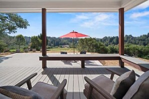 Eine überdachte Terrasse mit Holzmöbeln und einem roten Sonnenschirm, mit Blick auf eine bewaldete Landschaft.