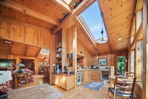 Ein Holzblockhaus-Interieur mit hoher Decke, Dachfenster, Küche, Essbereich und einem gemütlichen Wohnzimmer.