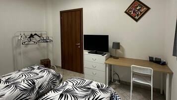 A bedroom with a bed, a desk, a chair, a TV, a door, and a ceiling light.