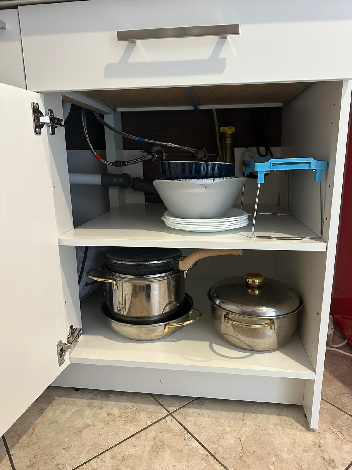 Ett köksskåp med kastruller, en diskho och en blå pall.