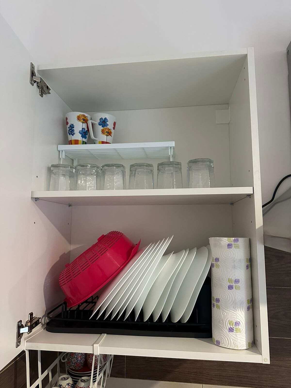 Keittiön yläkaappi, jossa on astiateline, pino lautasia ja rulla paperipyyhkeitä.