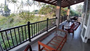 Un balcon abrité avec une table et des chaises en verre, une balustrade et une vue sur la verdure et les arbres.