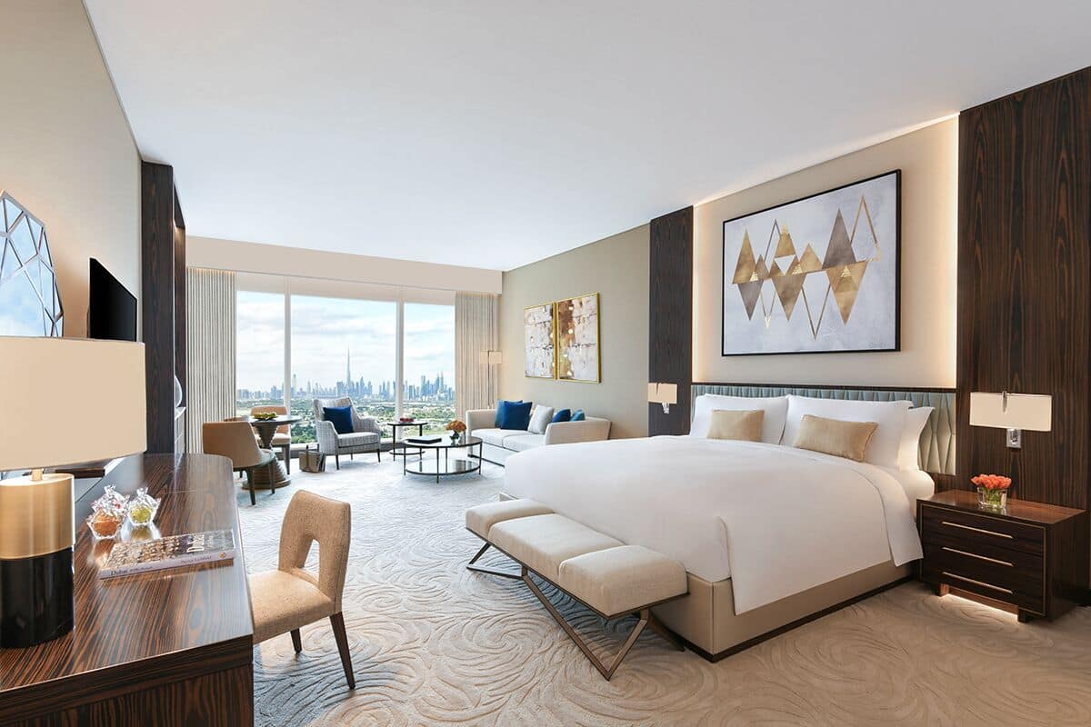Una habitación de hotel moderna con una cama grande, un escritorio, un rincón de descanso y vistas a la ciudad.