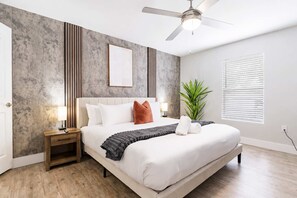 A bedroom with a bed, bedside tables, a ceiling fan, a potted plant, and a window with blinds. - South Tampa 2BR | 2 Kings, Pool, Gym & Parking (Tampa)